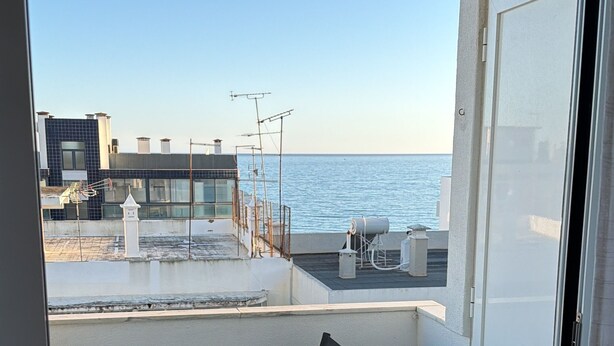 Een balkon met een tafel en stoelen, met uitzicht op een waterpartij en gebouwen.