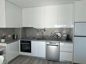 Eine moderne Küche mit weißen Schränken, einem Geschirrspüler, einem Backofen und einer Spüle.