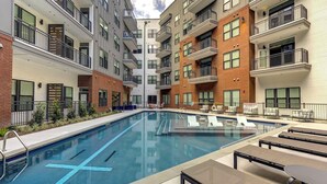 Un immeuble d’appartements moderne doté d’une piscine centrale, d’un espace extérieur aménagé et de nombreux balcons.