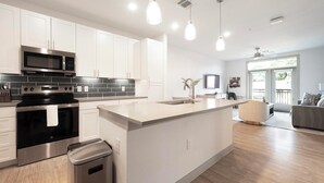 Une cuisine moderne avec des meubles blancs, des appareils en acier inoxydable et des luminaires suspendus.