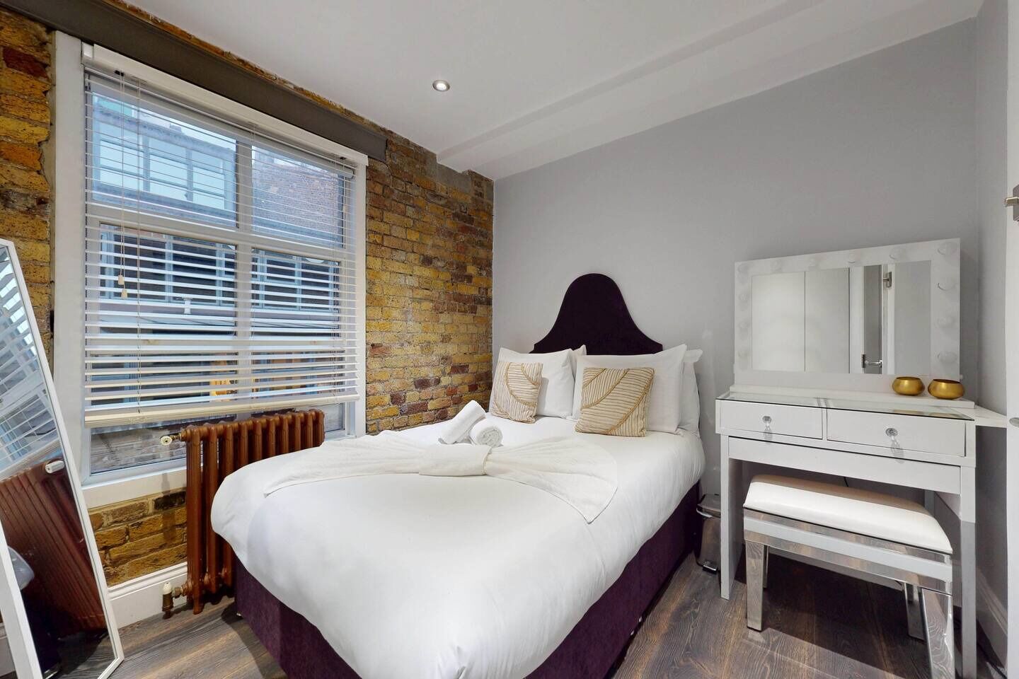 Een slaapkamer met een groot bed, een dressoir, een spiegel en een bakstenen muur.