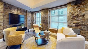 A modern living room with a stone wall, a flat-screen TV, and comfortable seating. - Stylish Penthouse with City Views and Aircon - Pass the Keys (London)