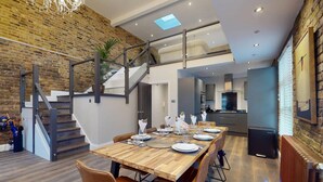A modern dining area with a wooden table set for four, a staircase, and a kitchen in the background. - Stylish Penthouse with City Views and Aircon - Pass the Keys (London)