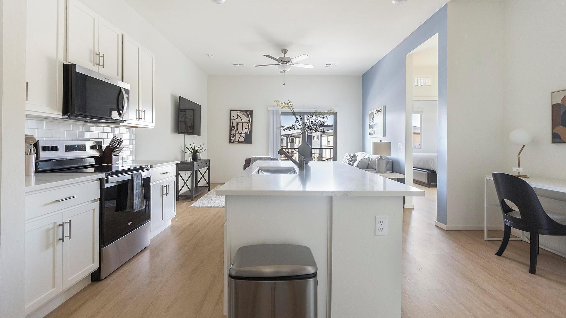 A modern kitchen with white cabinets, a stainless steel stove, and a large island with a sink.