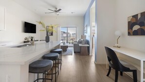 A modern kitchen with a central island, bar stools, a dining area with a table and chairs, and a view of the outside. - Landing | Modern 2BD, Pool (Casas Adobes)