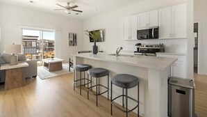 Een moderne keuken met witte kasten, een centraal eiland met krukken, een magnetron en een oven.
