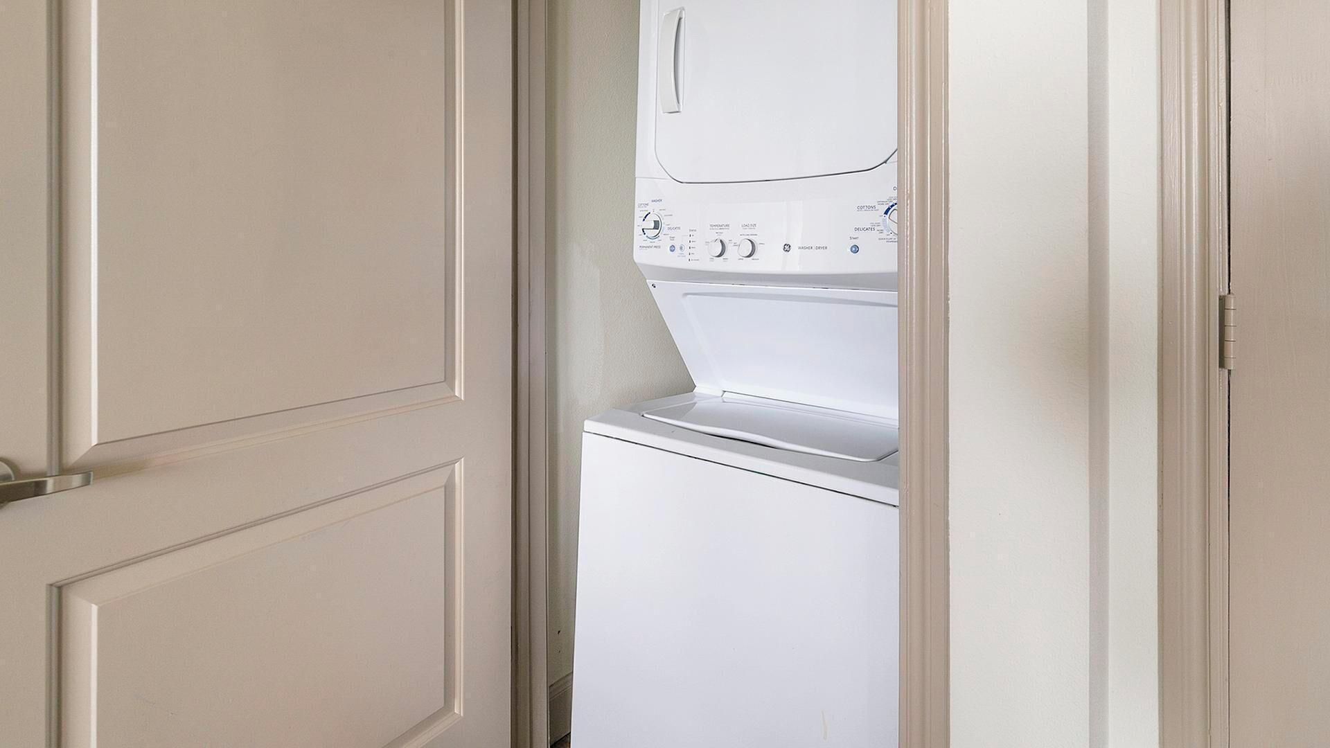 Un appareil combiné lave-linge et sèche-linge blanc, fixé au mur, doté de panneaux de commande et d’une porte.