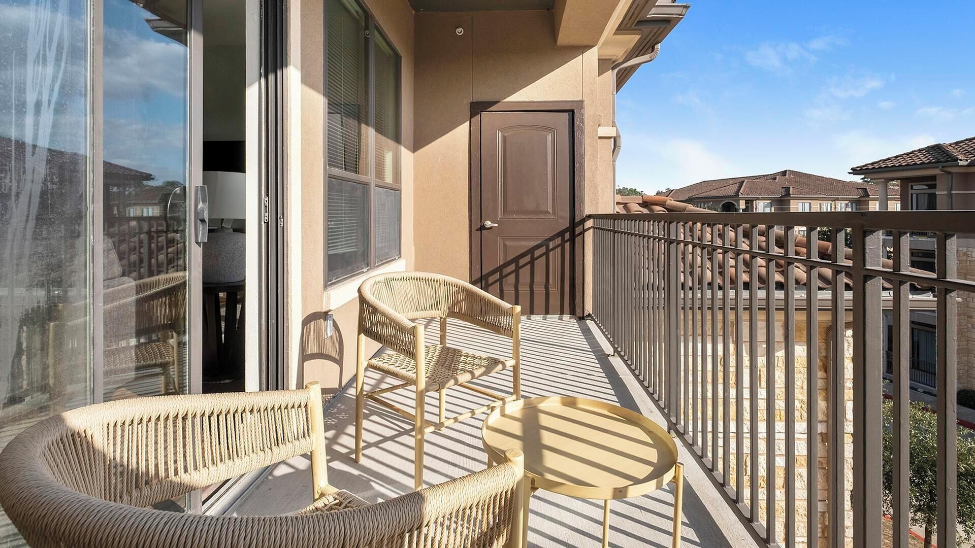 Een balkon met rieten stoelen, een klein tafeltje, een schuifdeur en een bruine deur.