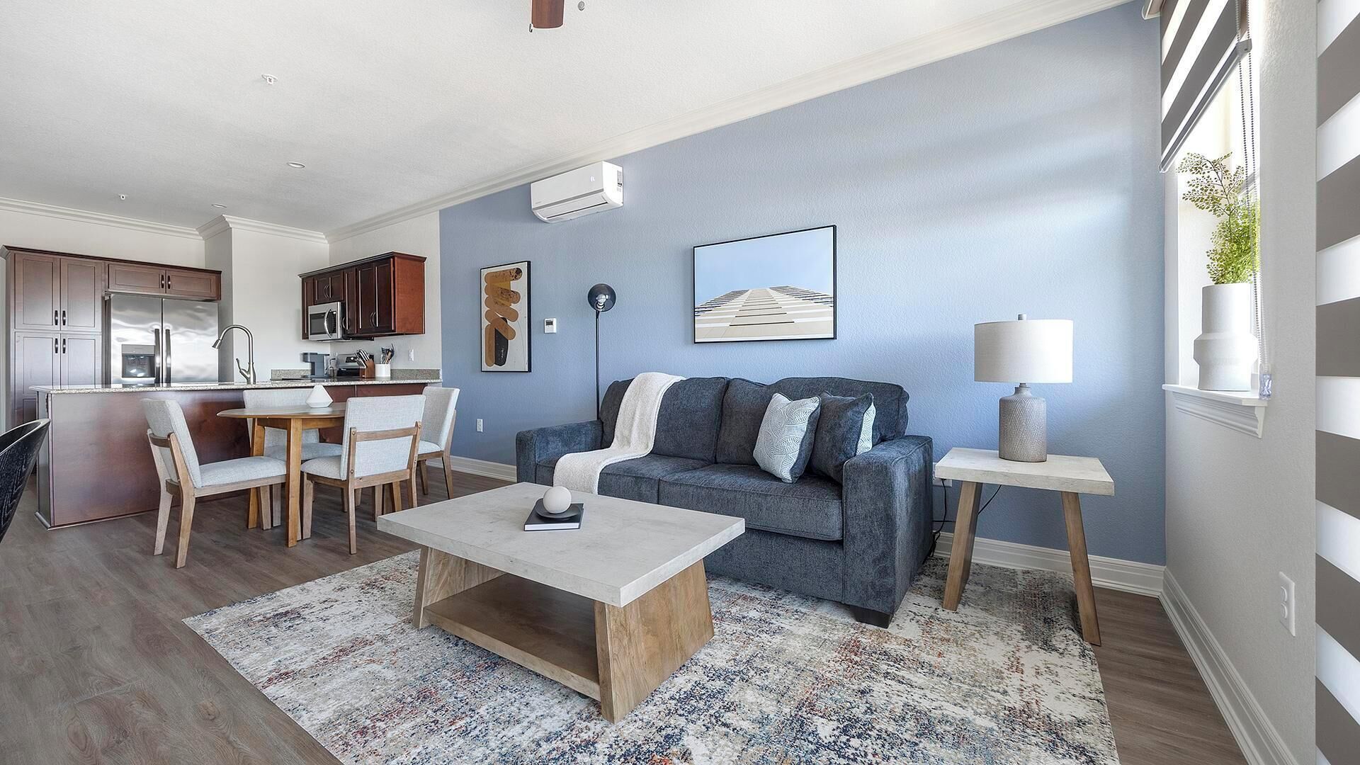 Una sala de estar moderna con un sofá gris, una mesa de centro y una zona de comedor con una cocina al fondo.