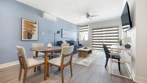Una sala de estar moderna con comedor, que incluye un sofá, una mesa de centro y un televisor montado en la pared.