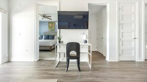 Una habitación moderna con piso de madera, un escritorio con silla, una cama con cabecera y un ventilador de techo.