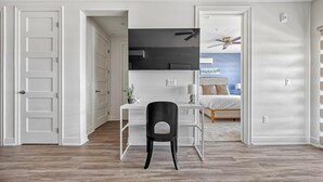 Ein Zimmer mit Schreibtisch, Stuhl, Bett und Deckenventilator.