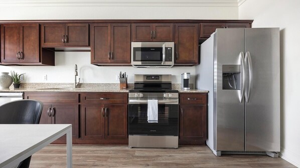 A modern kitchen with dark wooden cabinets, stainless steel appliances including a microwave, oven, and refrigerator, and a granite countertop.