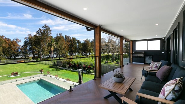 Ein moderner Außenbereich mit Pool, Holzterrasse und Blick auf einen Park mit Bäumen und einem See.