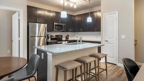 A modern kitchen with dark cabinets, stainless steel appliances, a granite countertop, and a bar area with stools. - Landing | Amazing 2BD, Gym, Game Room (Myrtle Beach)