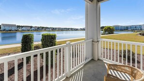 A balcony with a view of a lake, a white fence, and a wicker chair. - Landing | Amazing 2BD, Gym, Game Room (Myrtle Beach)