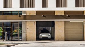 Moderni rakennus, jossa on autotalliin johtava sisäänkäynti, autotalliin pysäköity auto ja kyltti, jossa lukee: ”THE FLOODGATE”.