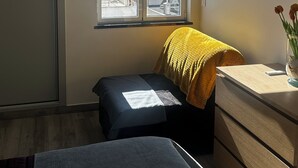 Quarto com janela vista para o mar, uma cama, um banquinho pequeno, um penteado e um ar condicionado.