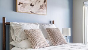 A neatly made bed with white linens and two patterned pillows, a bedside lamp, and a framed artwork on the wall. - Landing | Chic Studio, Rooftop Lounge, Pool (Springfield)