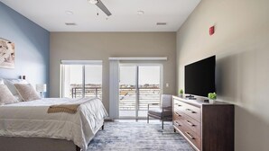 A modern bedroom with a large bed, a dresser, a TV, and a balcony with a view. - Landing | Chic Studio, Rooftop Lounge, Pool (Springfield)