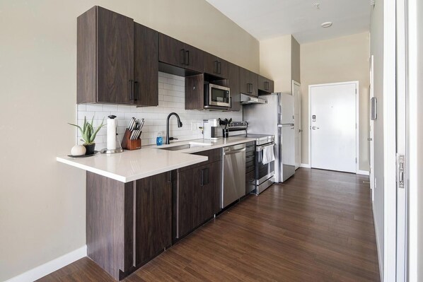 A modern kitchen with dark wood cabinets, stainless steel appliances, and a white countertop.