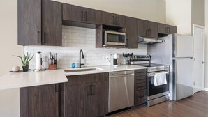 A modern kitchen with dark wood cabinets, a stainless steel dishwasher, a microwave, a stove, and a refrigerator. - Landing | Chic Studio, Rooftop Lounge, Pool (Springfield)