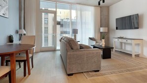 A modern living room with a sofa, a dining table, and a TV mounted on the wall. - Landing | Stunning 1BD, Yoga Studio, Gym (San Antonio)