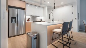 A modern kitchen with a stainless steel refrigerator, a central island with bar stools, and a trash bin. - Landing | Stunning 1BD, Yoga Studio, Gym (San Antonio)