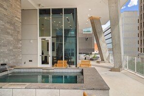 A modern indoor pool area with a glass wall, two wooden chairs, and a concrete pillar. - Landing | Stunning 1BD, Yoga Studio, Gym (San Antonio)