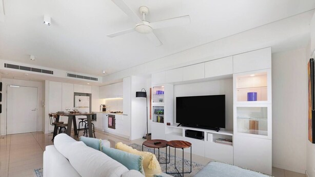 A modern living room with a sofa, a TV, and a kitchen in the background. - Lagoon Panorama Relaxed Waterfront Escape near CBD (Darwin)
