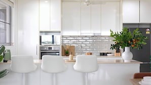 Una cocina moderna con armarios blancos, una isla central con taburetes de bar, un refrigerador y una planta en maceta.
