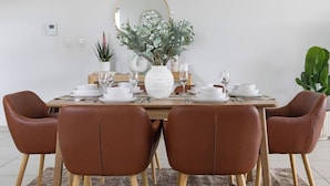 Una mesa de comedor dispuesta con platos blancos, vasos y un jarrón blanco con follaje.
