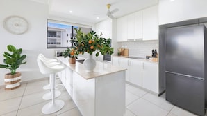 Una cocina moderna con armarios blancos, un refrigerador de acero inoxidable y una isla central con taburetes de bar.
