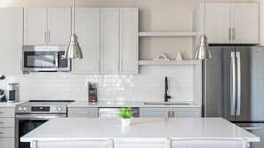 A modern kitchen with white cabinetry, stainless steel appliances, and pendant lighting. - Landing | Spectacular 2BD, Gym, Yoga Studio (Savannah)