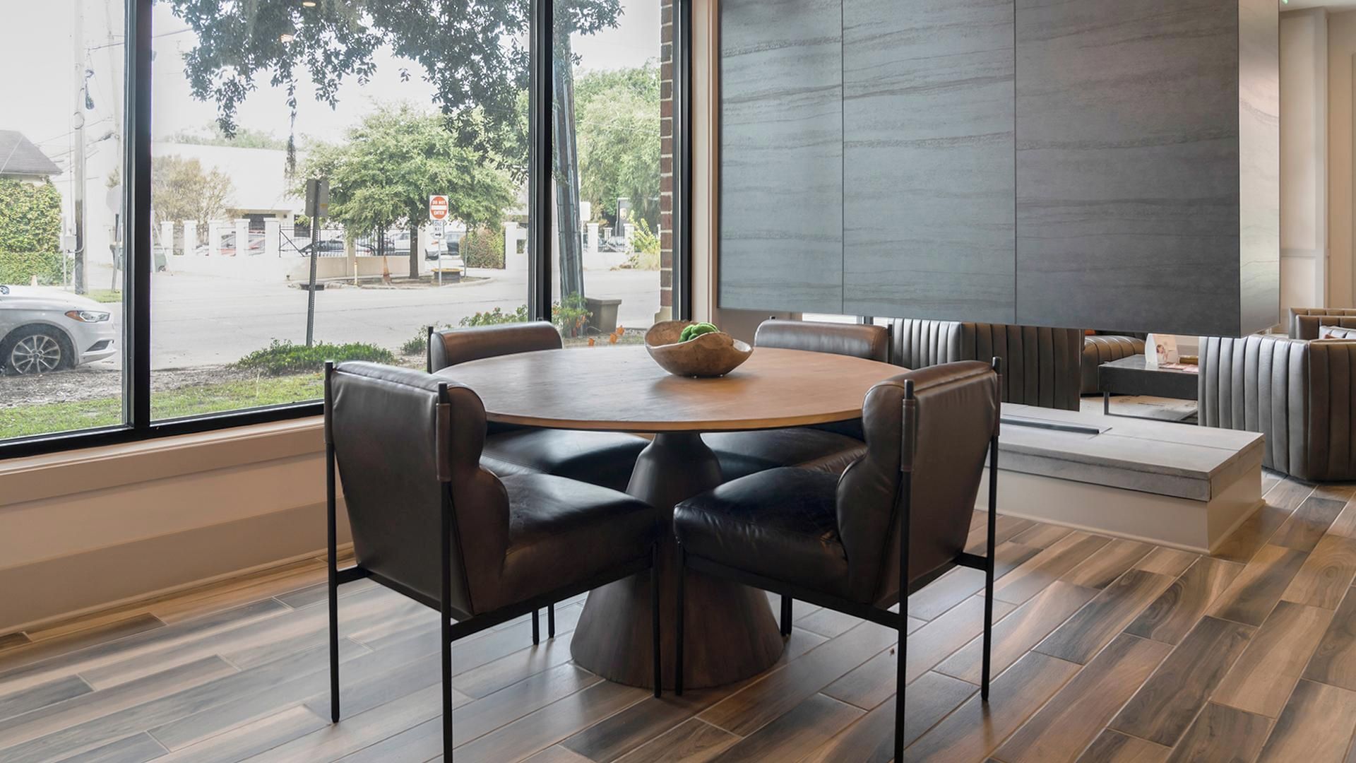 Un espace repas moderne avec une table ronde, des chaises en cuir noir et un saladier rempli de fruits.