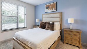 Quarto com uma cama grande, duas mesas de cabeceira, uma janela com persianas e uma obra de arte pendurada na parede.