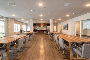 A conference room with long tables and chairs, a kitchen area, and large windows.