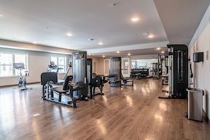 Ein geräumiger Fitnessraum mit unterschiedlichen Trainingsgeräten, großen Fenstern und Holzboden.
