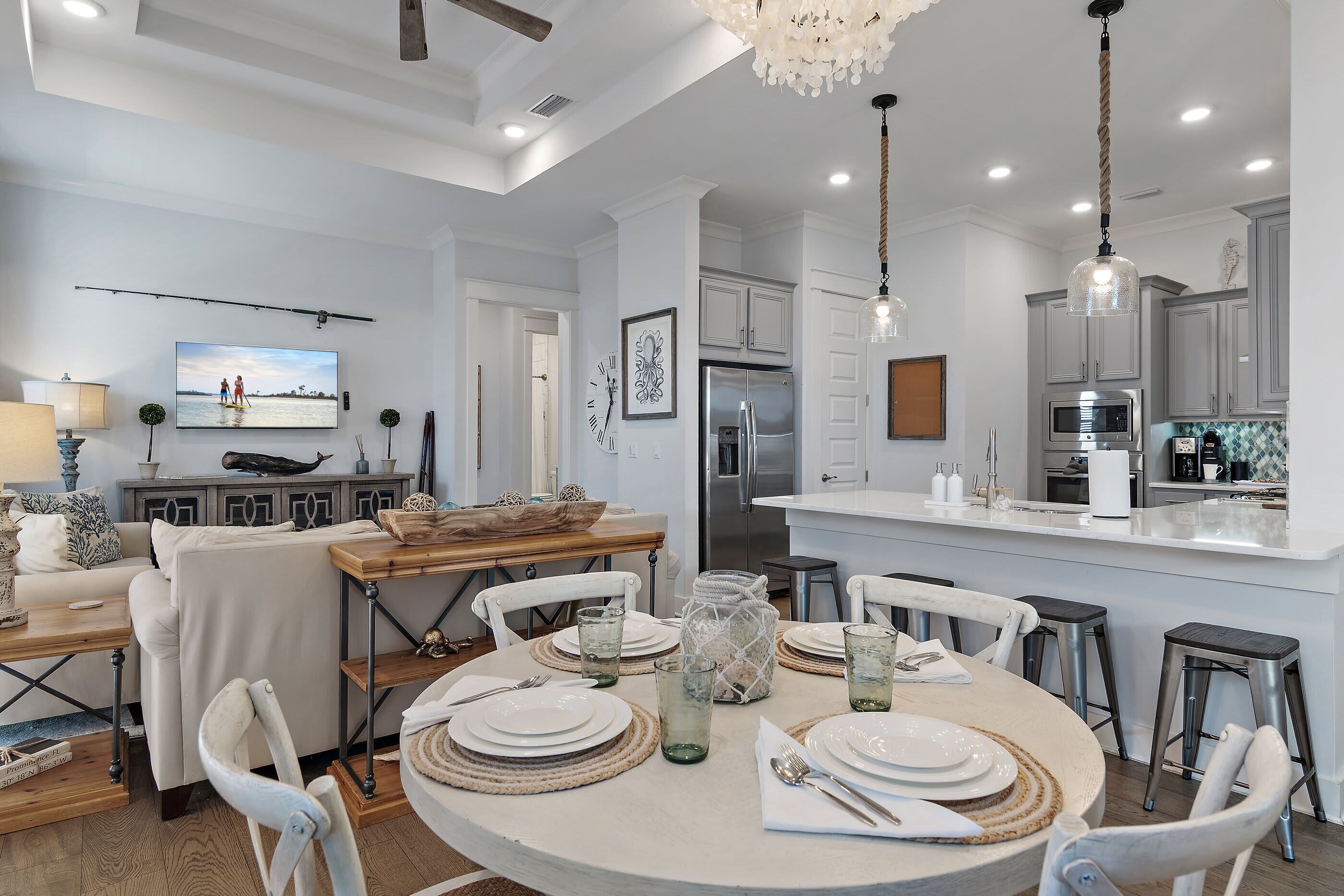 A modern kitchen with white cabinets, a stainless steel refrigerator, and a dining area with a round table set for four.