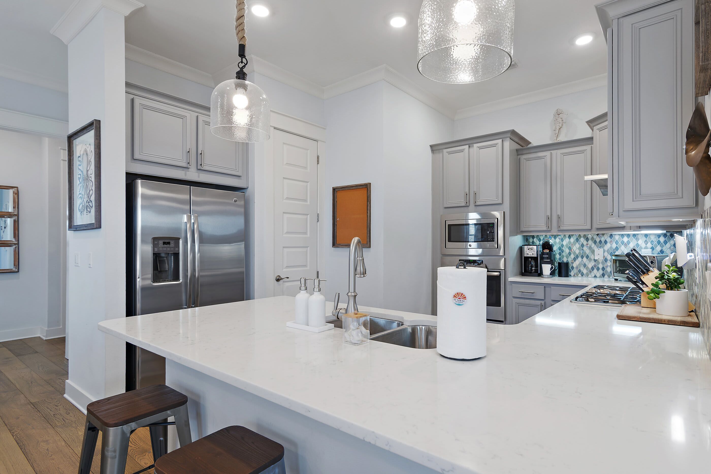 A modern kitchen with stainless steel appliances, a white marble countertop, and pendant lighting.