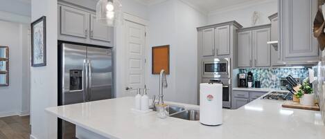 A modern kitchen with stainless steel appliances, a white marble countertop, and pendant lighting.