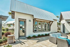 A modern house with a large window, a patio with a wicker sofa, and a metal roof. - Resort Pool + Cart | Steps to Big Chill on 30A (Watersound)
