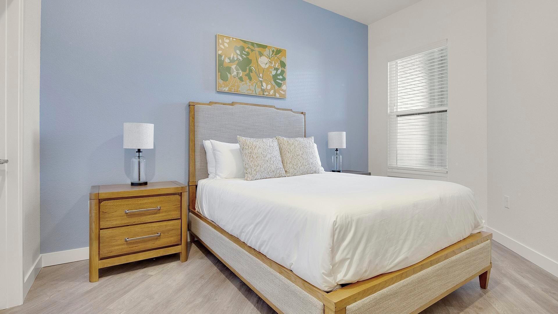 A bedroom with a bed, nightstands, a wall art piece, and a window with blinds.