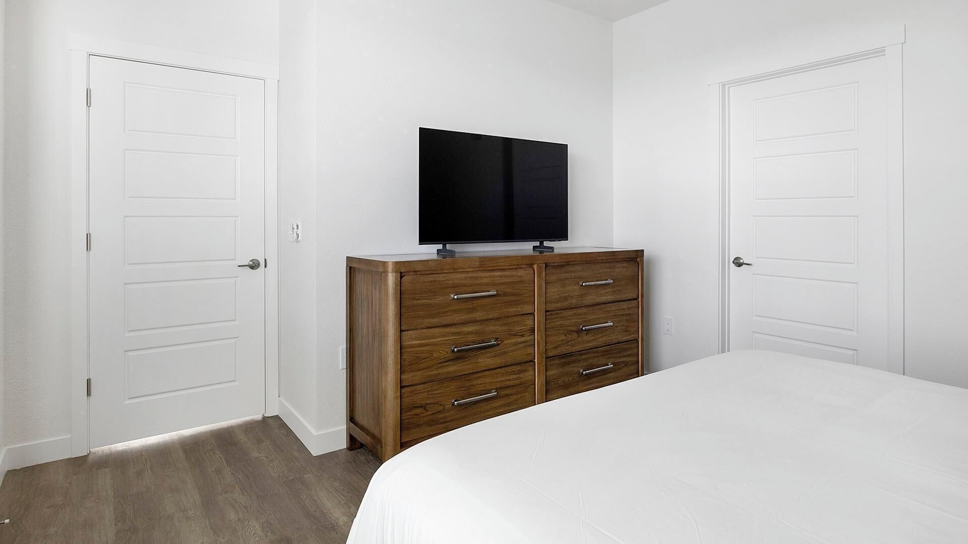A bedroom with a bed, a wooden dresser, and a TV mounted on the wall.
