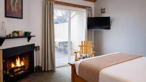 A cozy room with a fireplace, a bed, a TV mounted on the wall, and a view of the outdoors. - Black Butte Ranch Lodge Room 043 (Sisters)