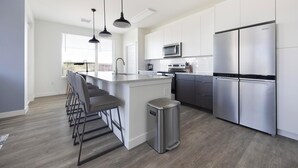 A modern kitchen with a central island, stainless steel appliances, and bar stools. - Landing | Stylish 2BD, Gym, Yoga Studio (Colorado Springs)