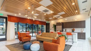 A modern lounge area with a sofa, armchairs, and ottomans, a kitchen area, and large windows offering a view of the outdoors. - Landing | Stylish 2BD, Gym, Yoga Studio (Colorado Springs)