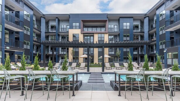 A modern apartment building with a rooftop pool area featuring lounge chairs and small trees. - Landing | Stylish 2BD, Gym, Yoga Studio (Colorado Springs)