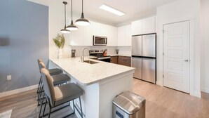 A modern kitchen with a central island, stainless steel appliances, and bar stools. - Landing | Chic 1BD, Yoga Studio, Gym (Colorado Springs)