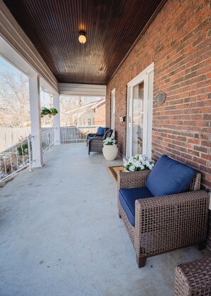 A covered porch with wicker furniture, a brick wall, and a hanging planter. - New listing! Historic 4 bedroom home in Russellville! (Russellville)